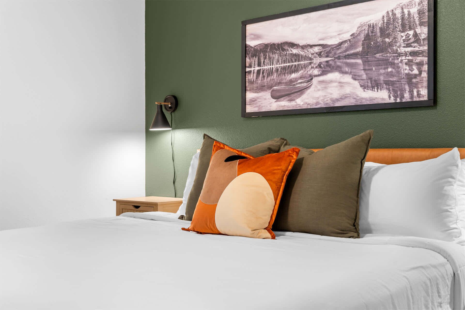 A neatly made bed with pillows, a nightstand with a lamp, and a framed picture on the wall.