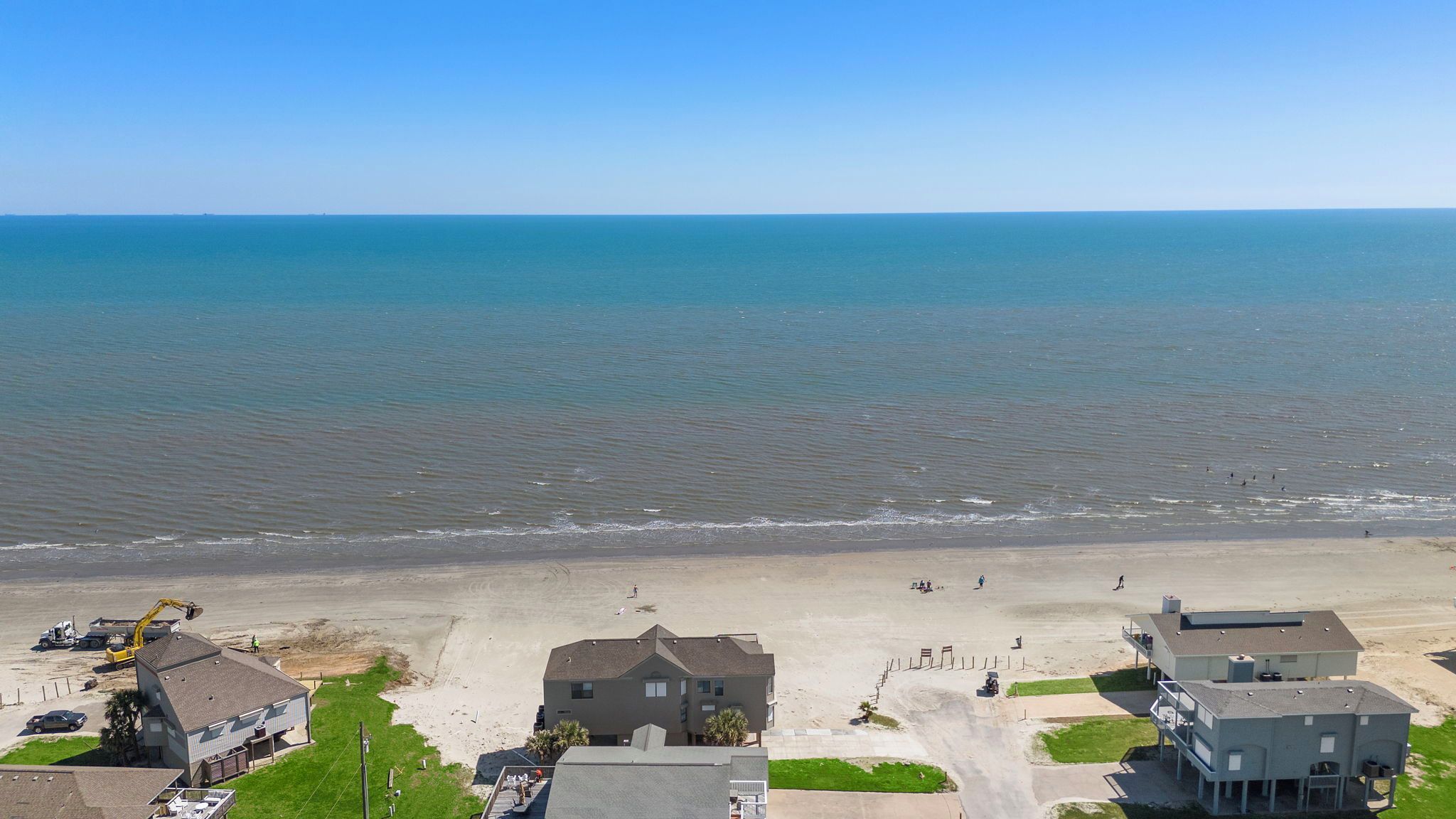 An aerial view of a coastal residential area with houses, a beach, and a clear blue sky.