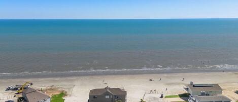 An aerial view of a coastal residential area with houses, a beach, and a clear blue sky.