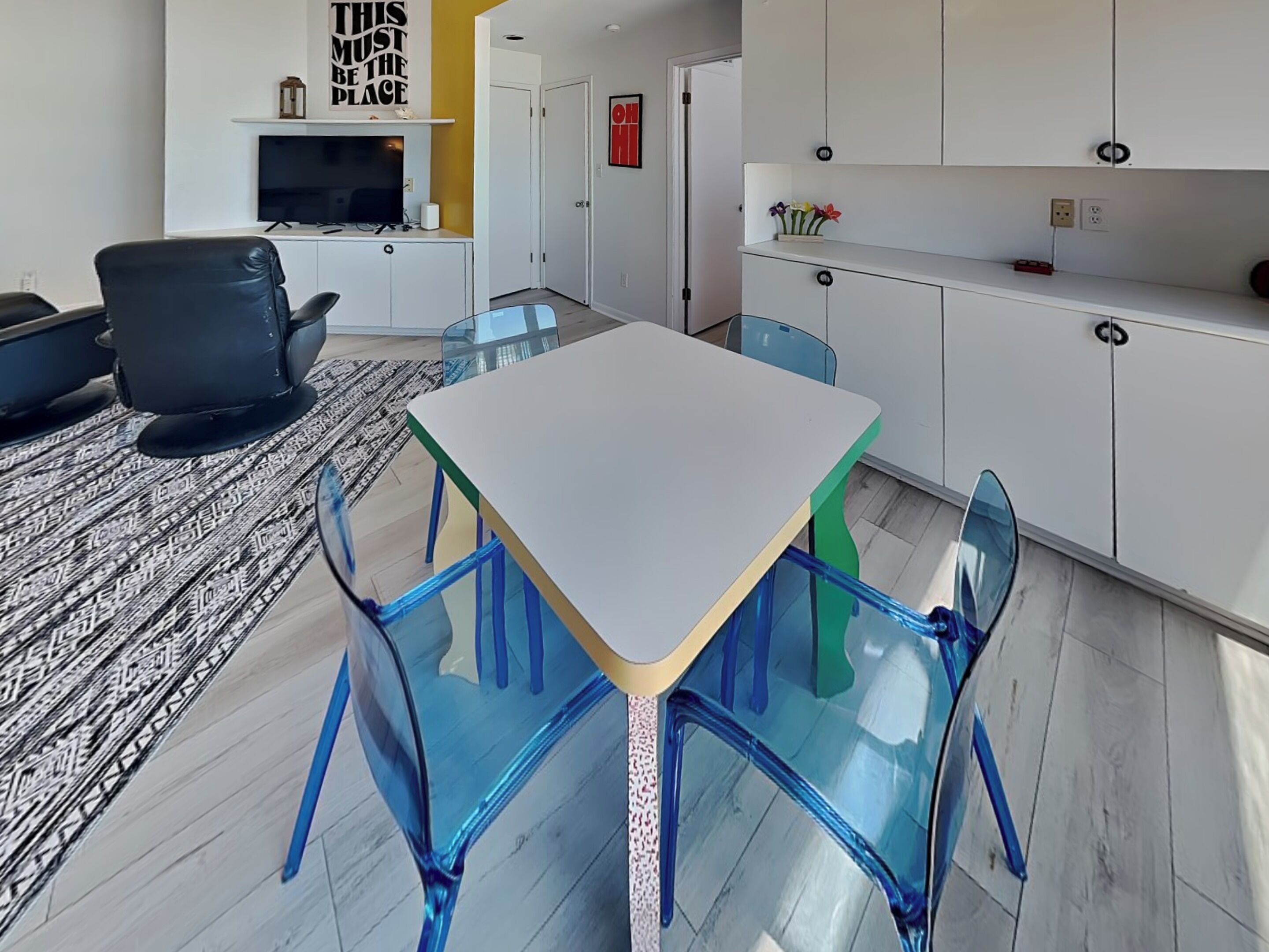 A modern kitchen with white cabinets, a white table, and blue chairs.