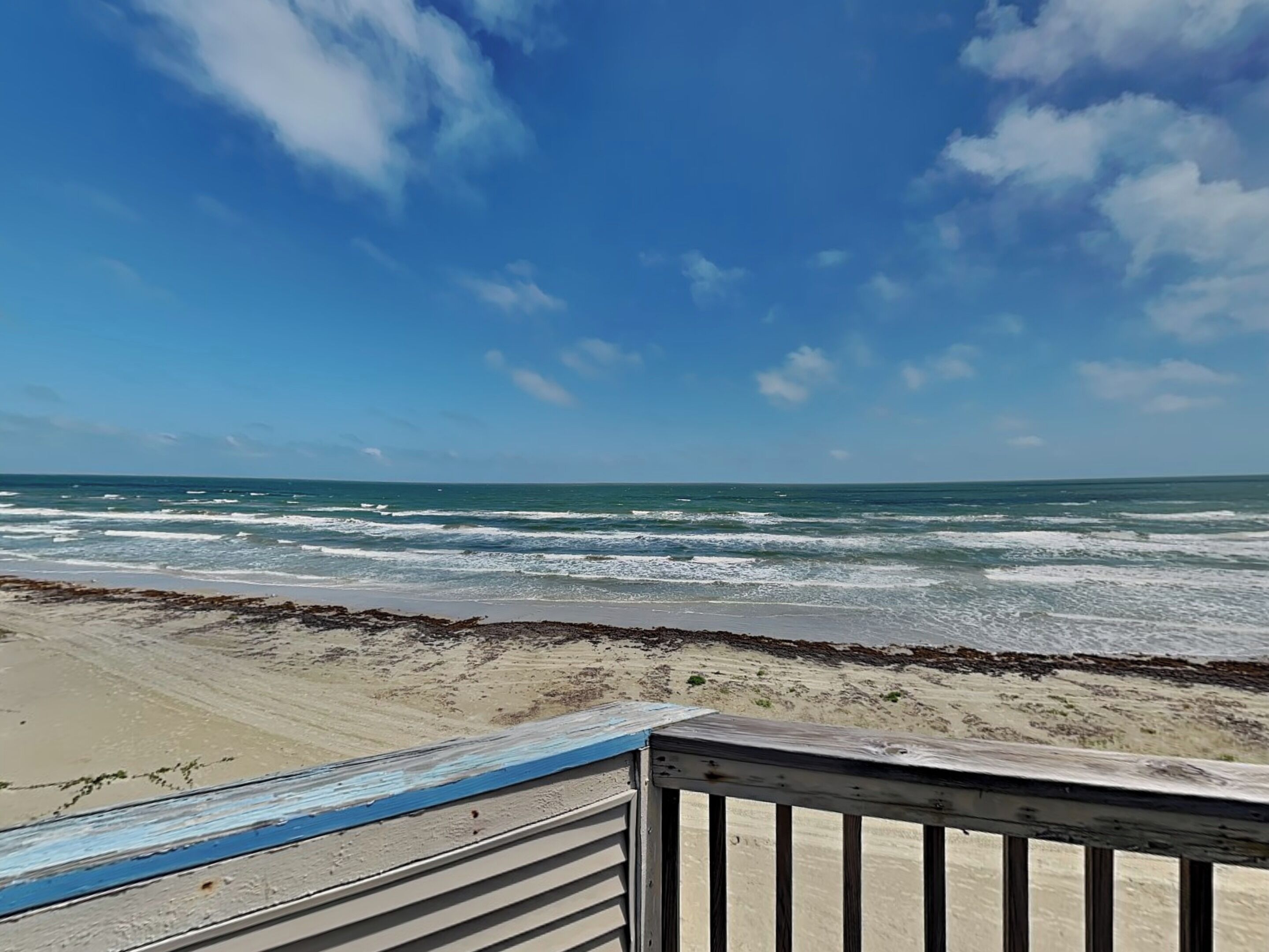 Uitzicht op een strand met golven, een houten terras en een heldere lucht.