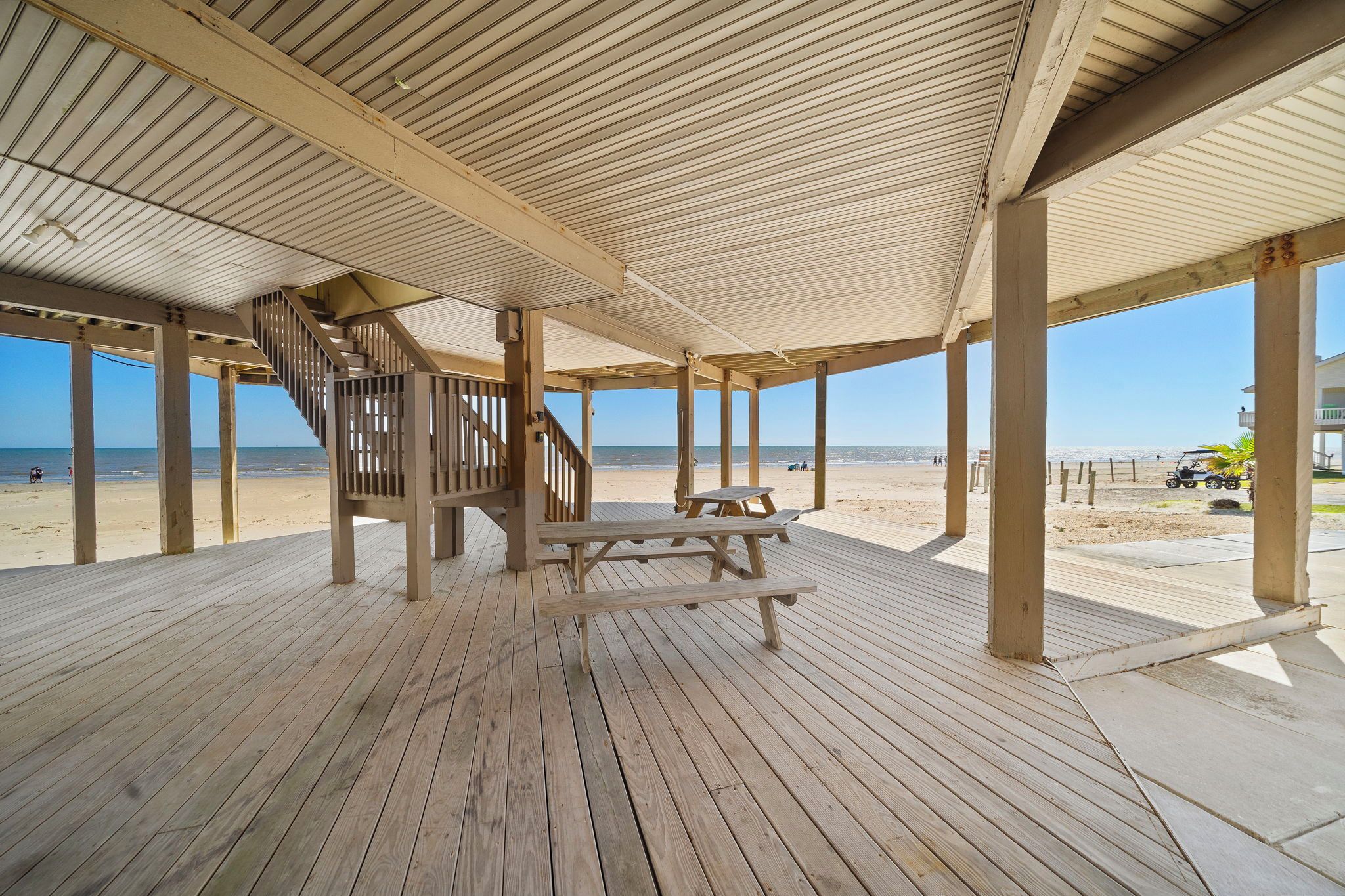 Una terraza de madera con mesas de picnic y una escalera que baja a la playa.