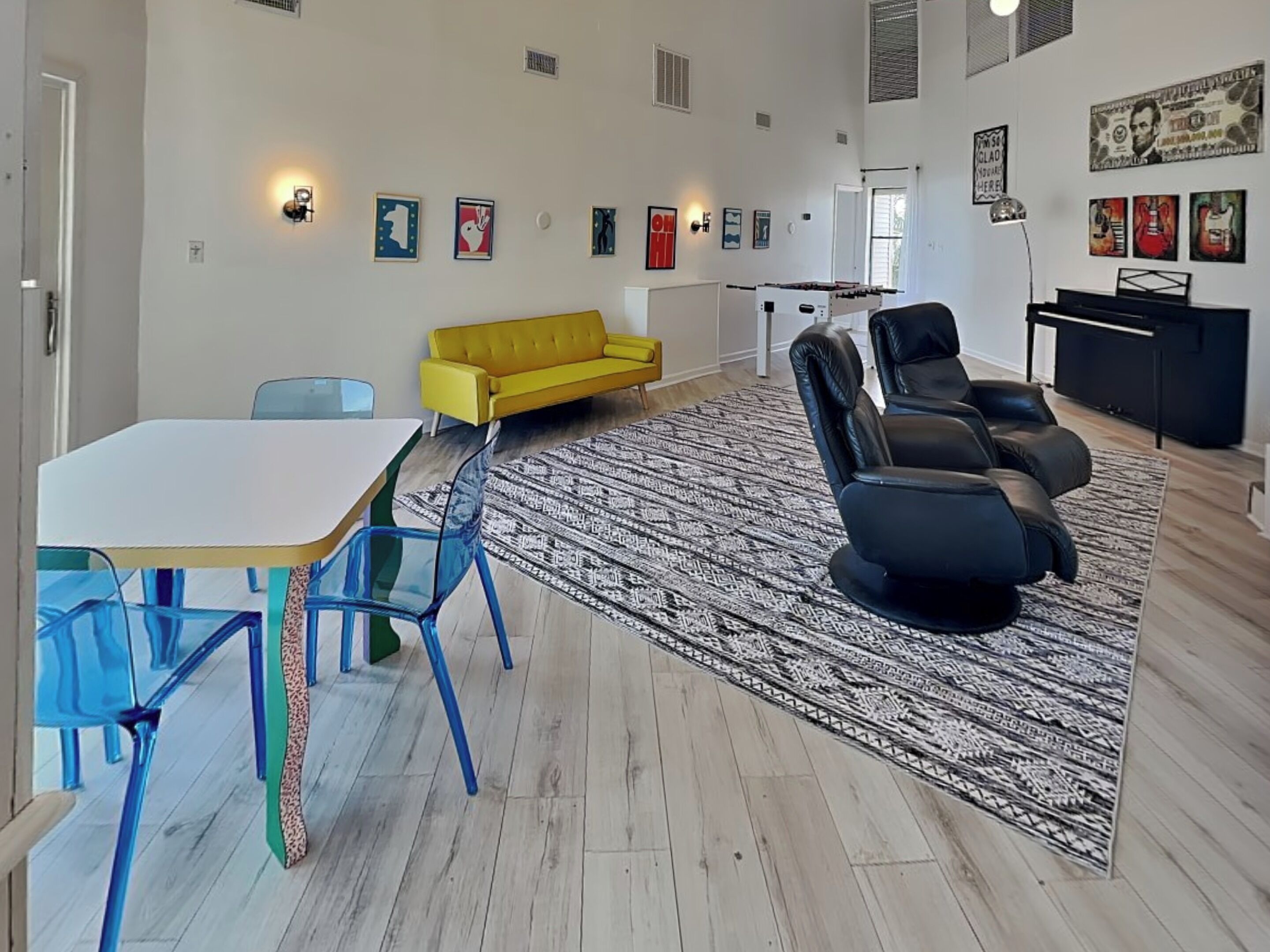 Una sala moderna con un sofá blanco, un sofá amarillo, un sofá negro, una mesa de comedor con sillas azules y una alfombra estampada.