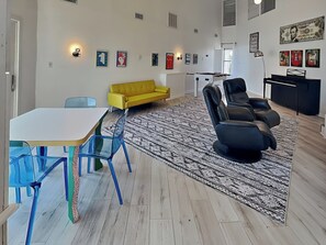 Un salon moderne avec un canapé blanc, un canapé jaune, un canapé noir, une table à manger avec des chaises bleues et un tapis à motifs.