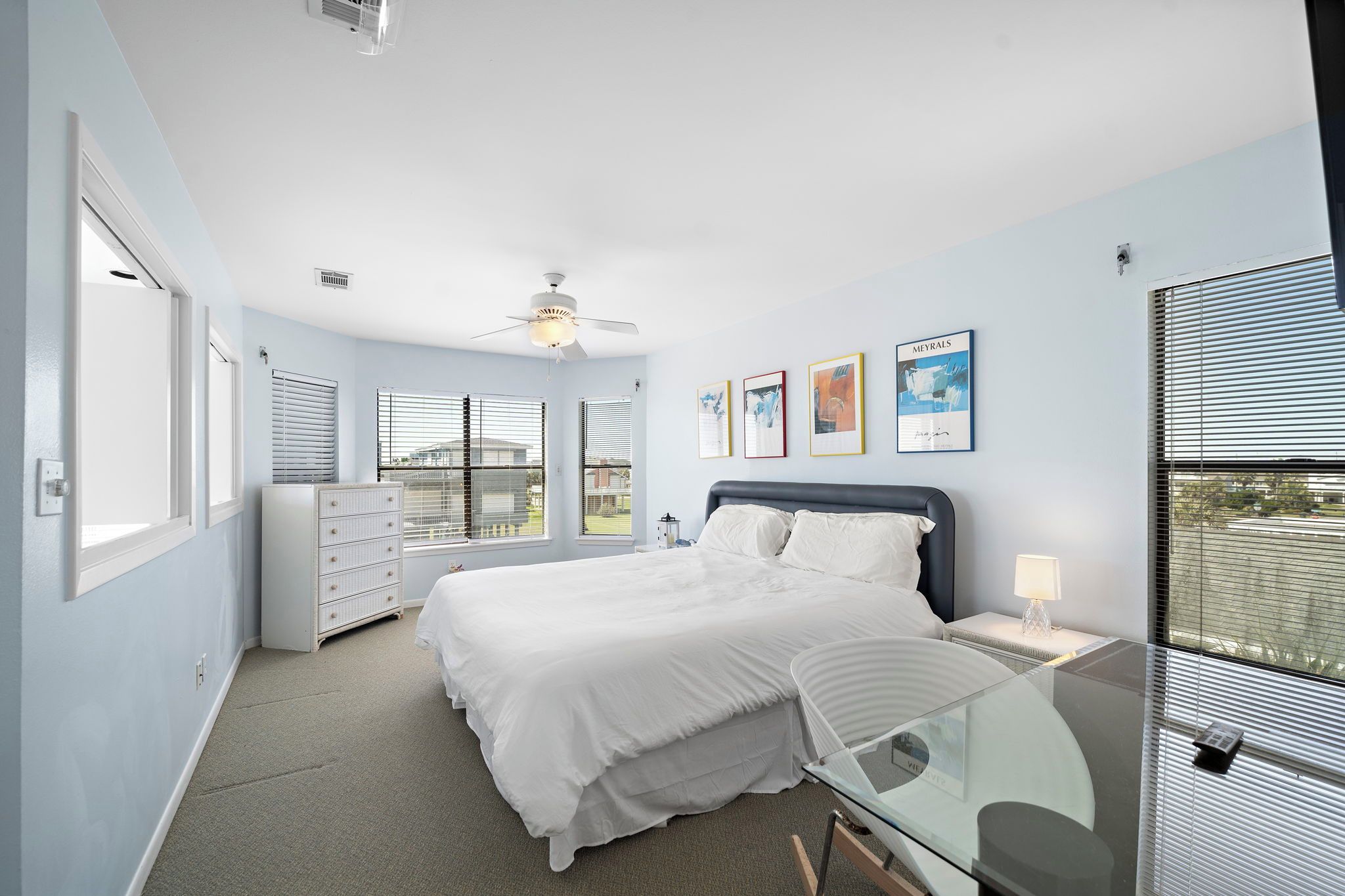 A bedroom with a bed, bedside table, lamp, ceiling fan, and a dresser.