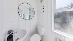 A bathroom with white tiles, a round mirror, a toilet, a sink, and a window with frosted glass. - Long Stay Ready | King Bed | Kitchen | WiFi | Town (Kent)