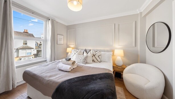 A bedroom with a large bed, bedside lamps, a round mirror, and a view of the outside. - Long Stay Ready | King Bed | Kitchen | WiFi | Town (Kent)