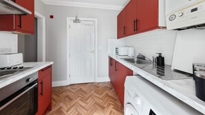 A compact kitchen with red cabinets, a white countertop, a built-in oven, and a microwave. - Long Stay Ready | King Bed | Kitchen | WiFi | Town (Kent)