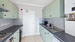 A kitchen with light green cabinets, a white door, a stainless steel sink, and a microwave. - Modern King Bed WiFi Kitchen Perfect for Long Stay (Kent)