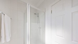 A bathroom with white tiles, a glass shower enclosure, and a white towel hanging on the wall. - Modern King Bed WiFi Kitchen Perfect for Long Stay (Kent)