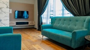 Uma sala de estar moderna com um sofá azul-turquesa, uma televisão e uma grande janela com cortinas.
