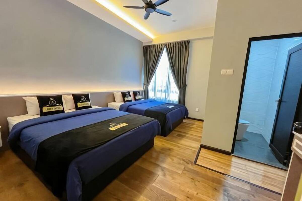 Een hotelkamer met twee bedden, een plafondventilator, een schuifdeur naar een balkon en een zichtbare badkamer.