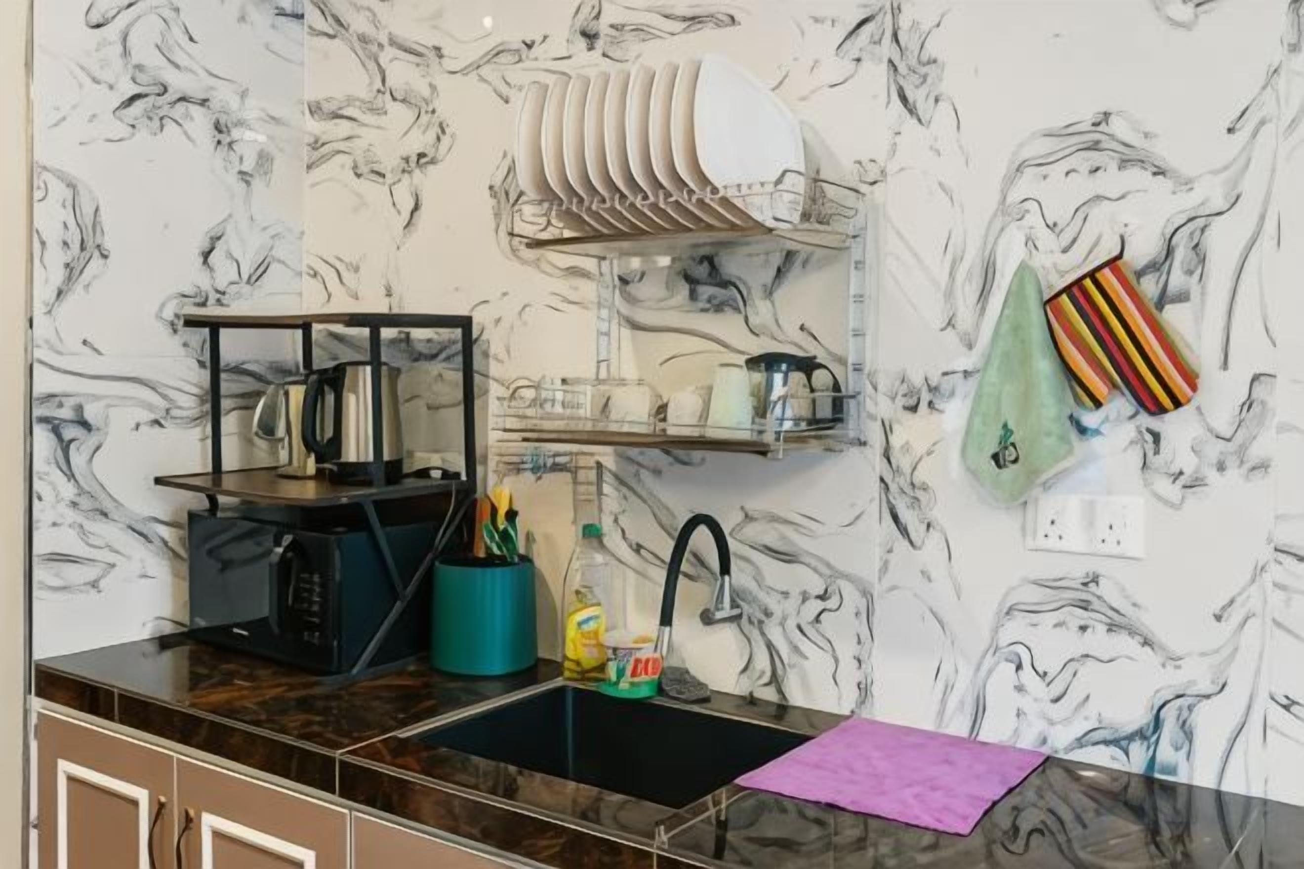 A kitchen with a marble backsplash, a black countertop, a sink, and a dish rack.