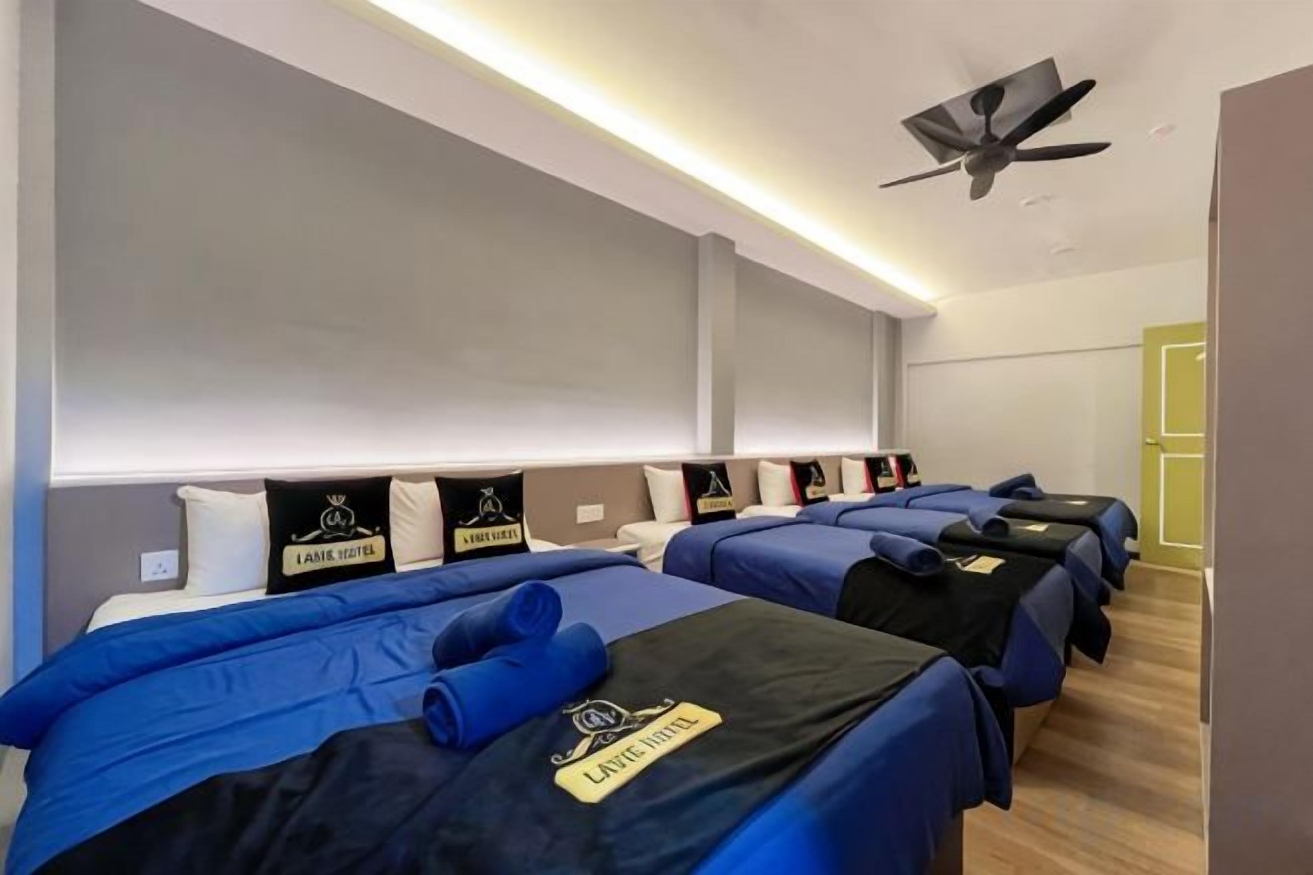 Een hotelkamer met meerdere bedden, een plafondventilator en een minibar.