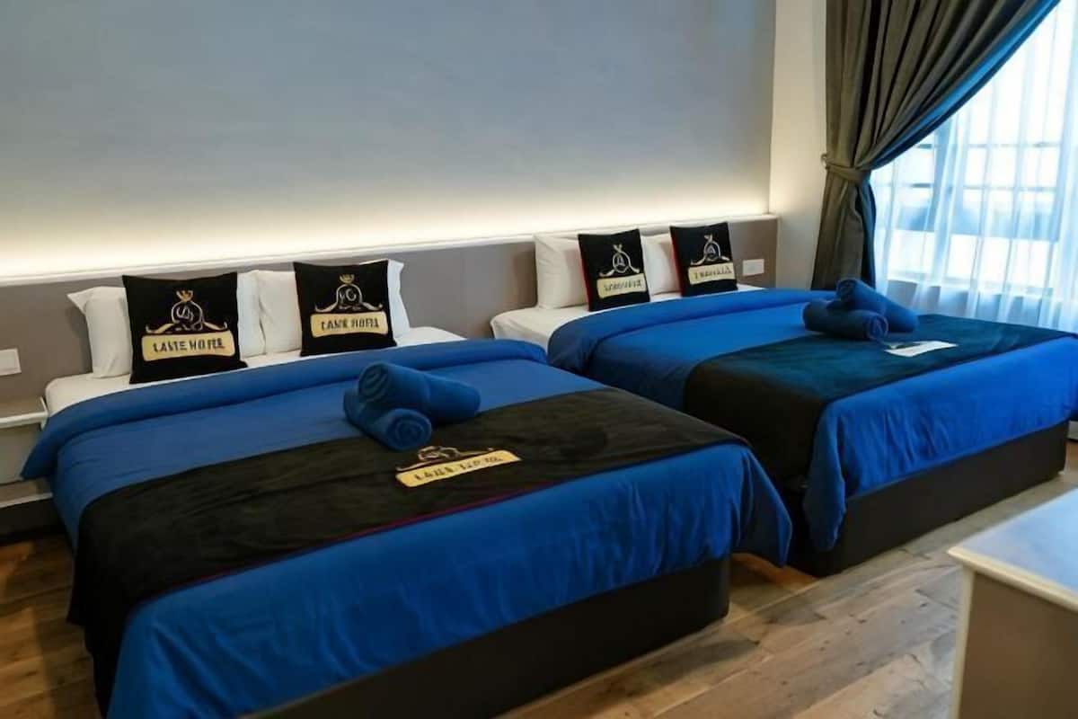 Een hotelkamer met twee bedden, elk met een blauwe spreidek en passende kussens, een nachtkastje en een raam met gordijnen.