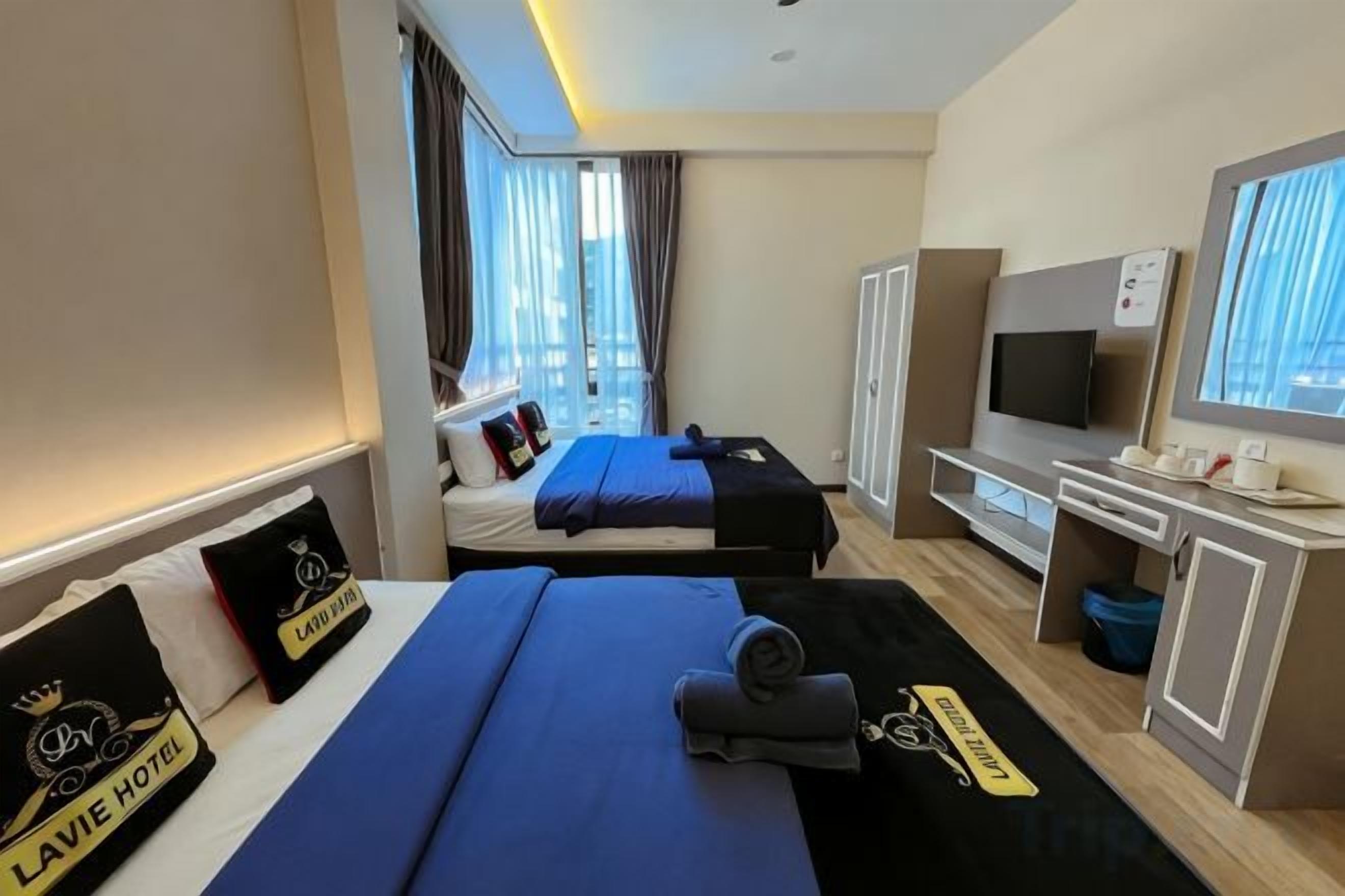 A hotel room with two beds, a desk with a computer, a TV, and a window with curtains.
