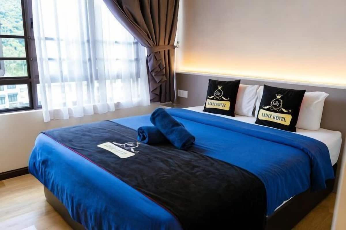 Een hotelkamer met een groot bed, twee kussens met logo's, een raam met gordijnen, en een bord aan de muur.