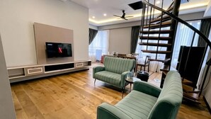Uma sala de estar moderna com uma TV de tela plana, sofás verdes, piso de madeira e uma escada.