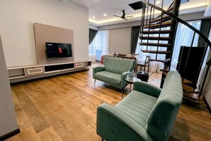 Ein modernes Wohnzimmer mit Flachbildfernseher, grünen Sofas, einer Treppe und einem Essbereich.