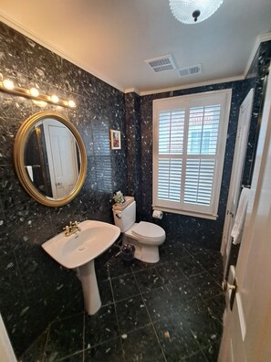 Une salle de bain avec un sol en marbre, un lavabo, des toilettes et une fenêtre avec des stores.