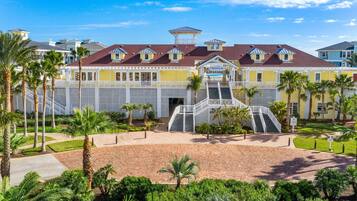 A beachfront hotel with a central staircase, palm trees, and a beach club sign.