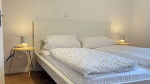 Un dormitorio minimalista con una cama blanca, dos mesitas de noche con lámparas y suelo de madera.