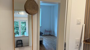Un pasillo con piso de madera, una puerta blanca y un ventanal pequeño.