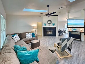 A modern living room with a sectional sofa, a fireplace, a ceiling fan, and a TV. - Rivers Edge Retreat by Distinctive Beach Rentals (St. Augustine)