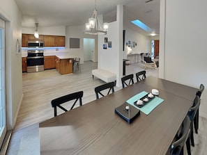A modern kitchen with stainless steel appliances, a wooden island, and a dining area with a dark wood table and black chairs. - Rivers Edge Retreat by Distinctive Beach Rentals (St. Augustine)
