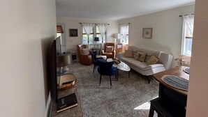Una sala de estar con sofá, sillas, una mesa de centro, televisor y lámpara.
