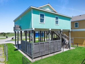 A two-story building with a covered porch and a staircase leading to the upper level. - Anchors Away-Sleeps 10, Fully Fenced Back Yard, Play Set, Walk to Beach, Pets OK (Bolivar Peninsula)