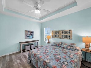 A bedroom with a bed, a nightstand, a ceiling fan, a window with blinds, and a wall-mounted artwork. - Anchors Away-Sleeps 10, Fully Fenced Back Yard, Play Set, Walk to Beach, Pets OK (Bolivar Peninsula)