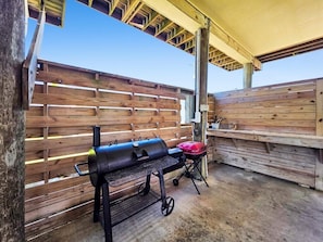 An outdoor barbecue area with a grill and a portable smoker, surrounded by wooden fences.