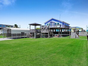 A large house with a covered outdoor area and a grassy lawn. - Ibis Isle-Bolivar Peninsula, Sleeps 12, Fenced Side Yard, Walk to Beach, In Town (Bolivar Peninsula)