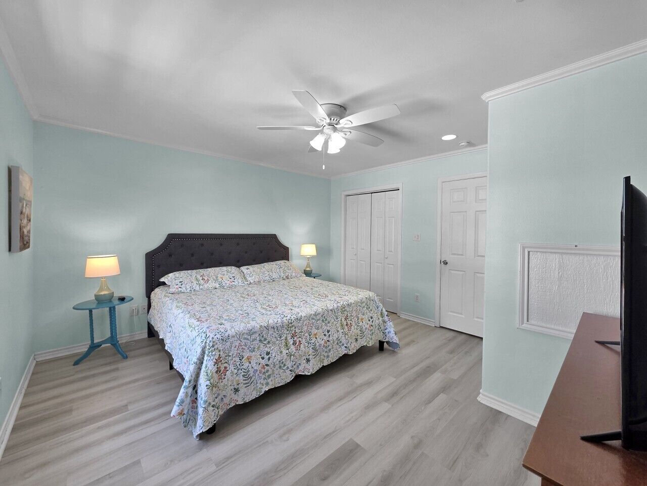 A bedroom with a bed, a ceiling fan, a nightstand, a lamp, and a television.