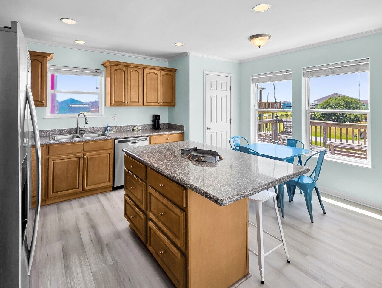A kitchen with wooden cabinets, a granite countertop, and a dining area with blue chairs.