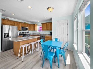 A modern kitchen with a central island, bar stools, and a dining table with chairs. - Ibis Isle-Bolivar Peninsula, Sleeps 12, Fenced Side Yard, Walk to Beach, In Town (Bolivar Peninsula)