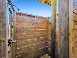 A wooden cabin with a sloped roof, a door with a metal handle, and visible plumbing pipes.
