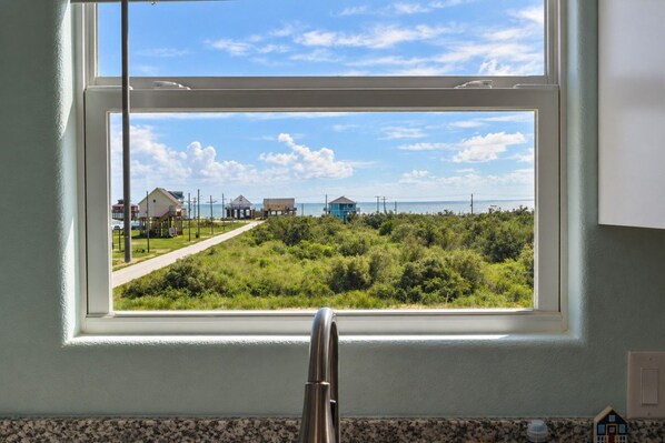 A window with a view of a coastal area, including a road and buildings.