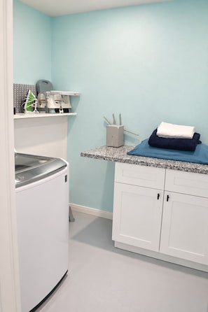 A laundry room with a washing machine, a drying rack, and a countertop with a towel and a container.