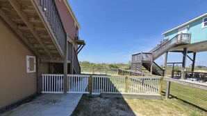 A building with a wooden deck, a white fence, and a clear sky. - Crabby Cove - Fully Fenced Side Yard, Pets OK, Gulf & Bay Views, Walk to Beach (Bolivar Peninsula)