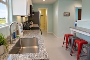 A kitchen with granite countertops, stainless steel sink, and red bar stools.