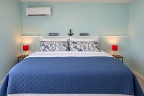 Un lit recouvert d’une courtepointe bleue matelassée, deux oreillers à motifs floraux et deux lampes de chevet avec des abat-jour rouges.