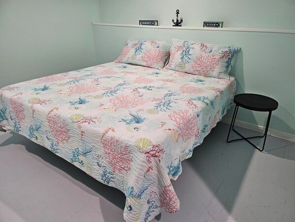 A bed with a floral quilt, a small black stool, and two signs on the wall reading "Serenity" and "Ocean".