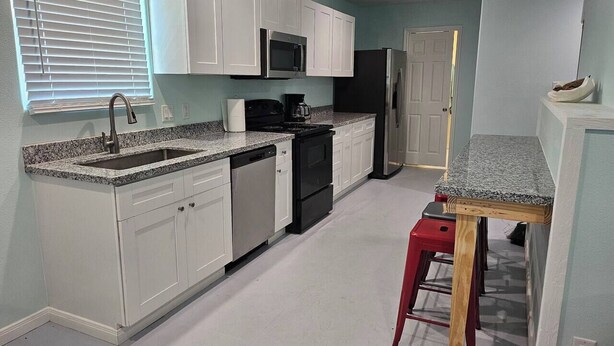 A kitchen with white cabinets, a microwave, a stove, and a refrigerator. - Crabby Cove - Fully Fenced Side Yard, Pets OK, Gulf & Bay Views, Walk to Beach (Bolivar Peninsula)