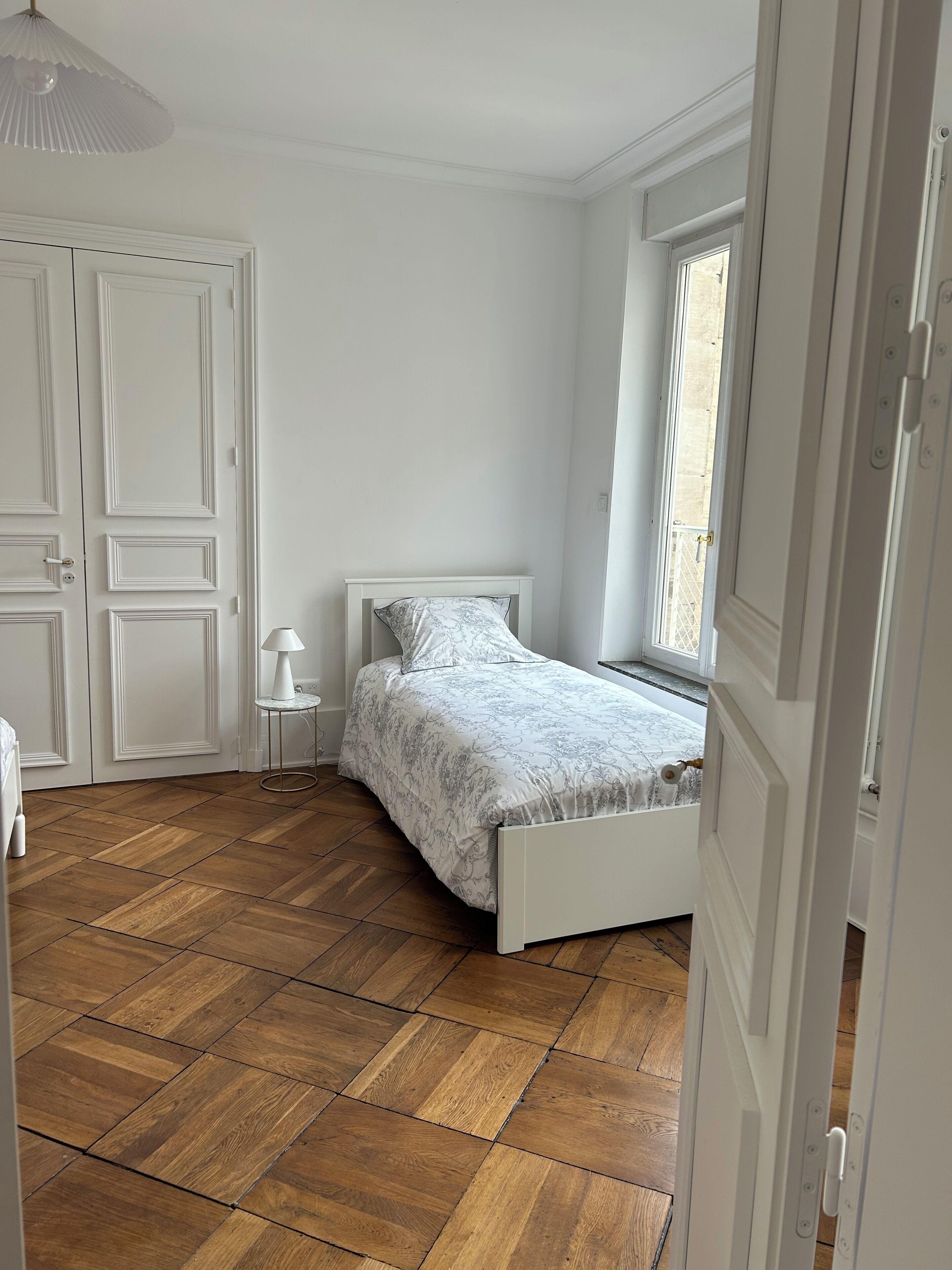 A bedroom with a bed, a nightstand, a lamp, and a window.