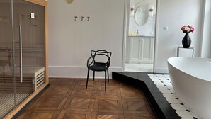 A modern bathroom with a glass shower enclosure, a black chair, a white vanity with a marble mirror, and a vase of flowers.