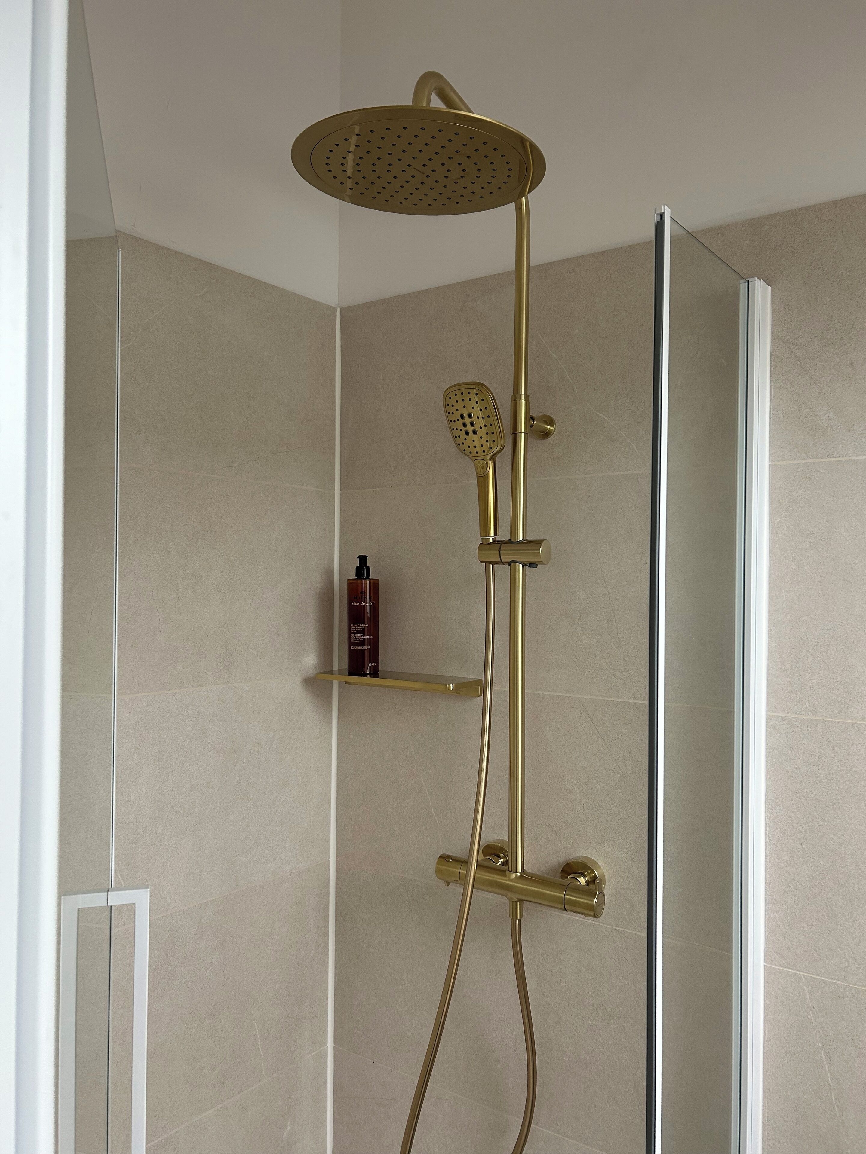Een douche met gouden afwerking, een handdouche en een douchelager aan de muur.