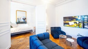 A modern hotel room with a bed, a large mirror, a blue sofa, a small round table, and a large painting on the wall.