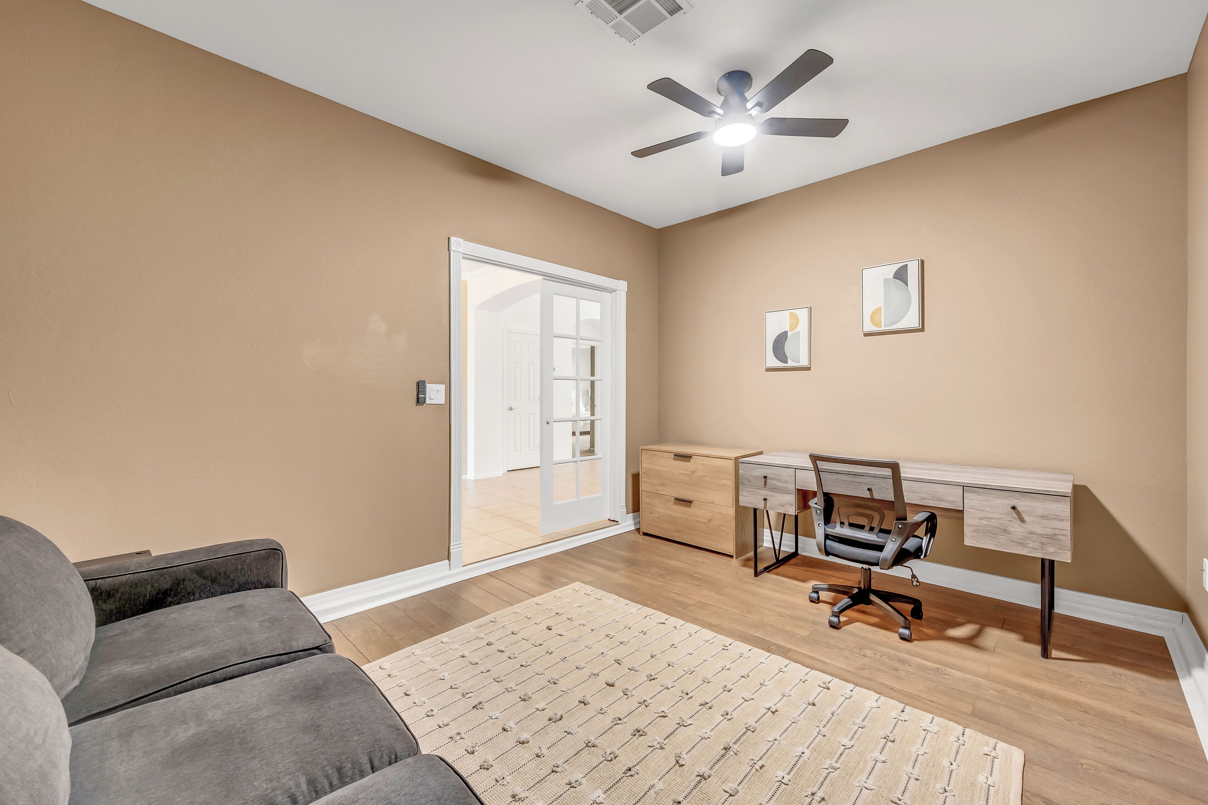 A modern living room with a gray sofa, wooden desk, and a ceiling fan.
